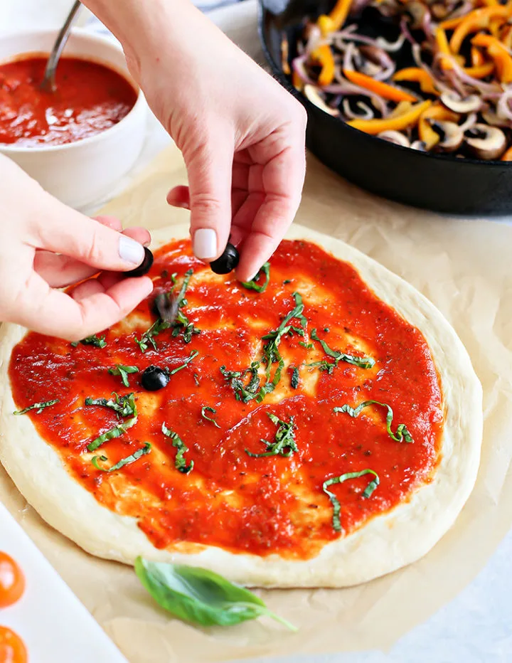 photo of woman adding fresh basil to a veggie pizza