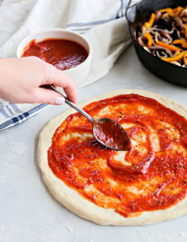 photo of a woman spreading sauce on a veggie pizza