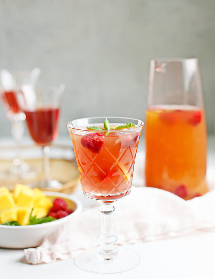 photo of a glass of rosé sangria with a pitcher of raspberry mango sangria and a bowl of fruit