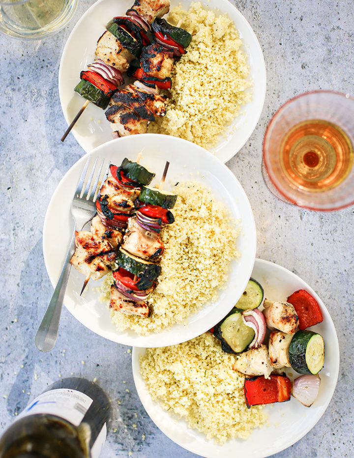 plates with grilled chicken kebabs and couscous on a table with glasses of wine