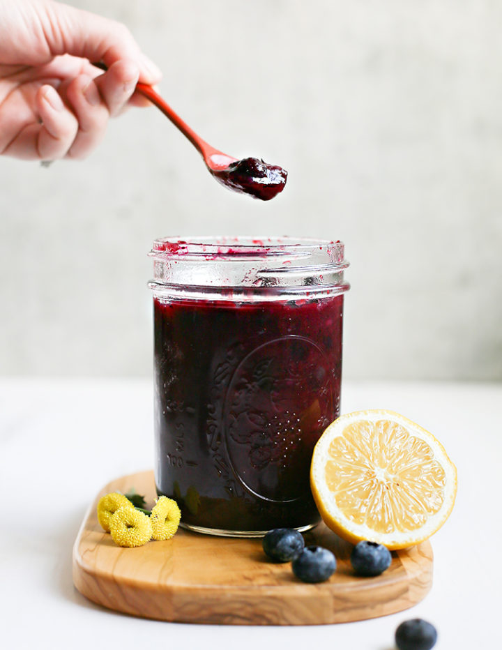 lemon blueberry sauce in a jar on a cutting board with a lemon and blueberries