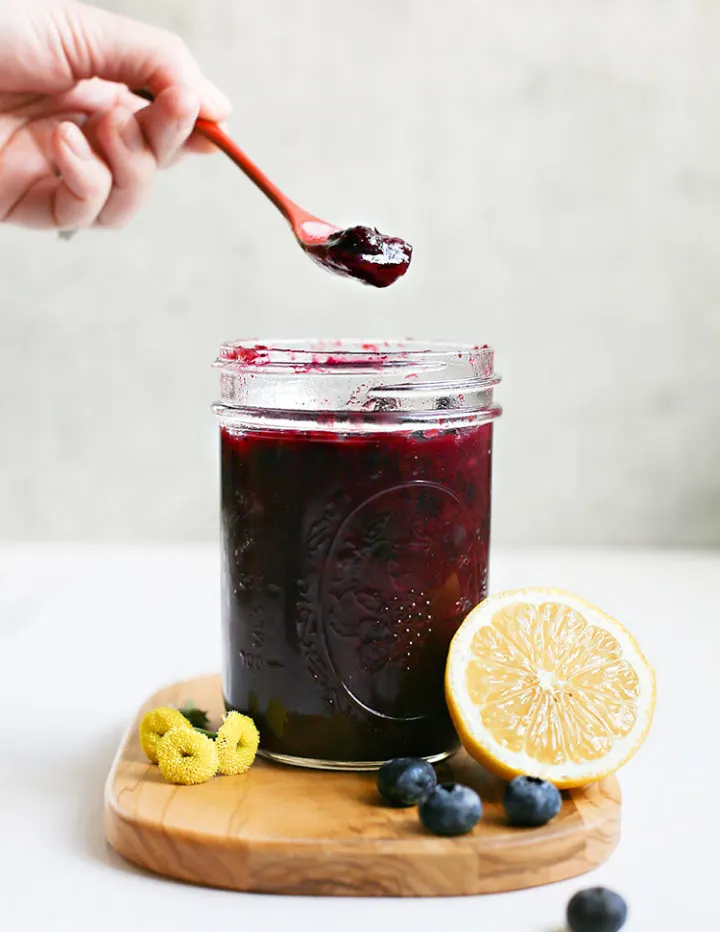 lemon blueberry sauce in a jar on a cutting board with a lemon and blueberries