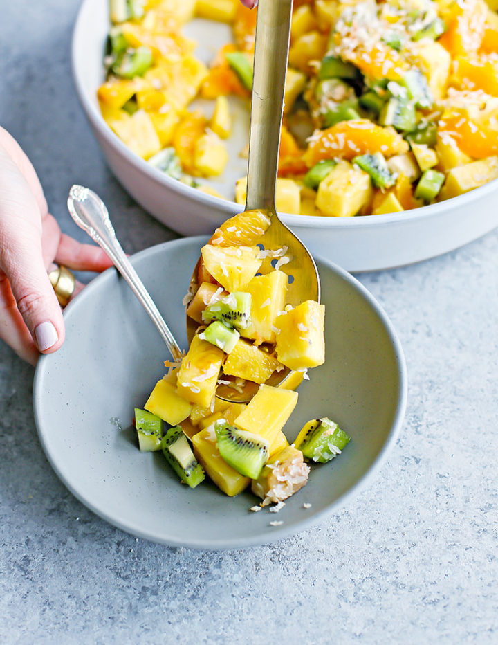 a photo of a woman serving tropical fruit salad into a small bowl