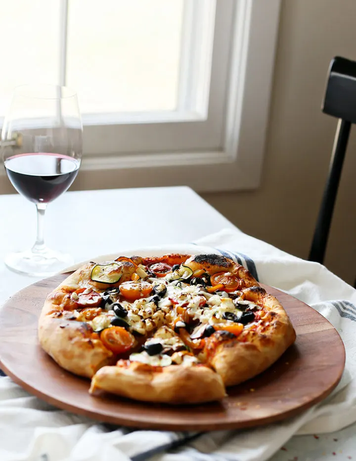 photo of a vegetarian pizza on a kitchen table with a glass of wine