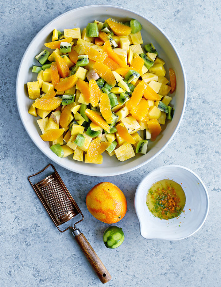 a photo of tropical fruits in a bowl next to a bowl of honey lime dressing for the fruit salad