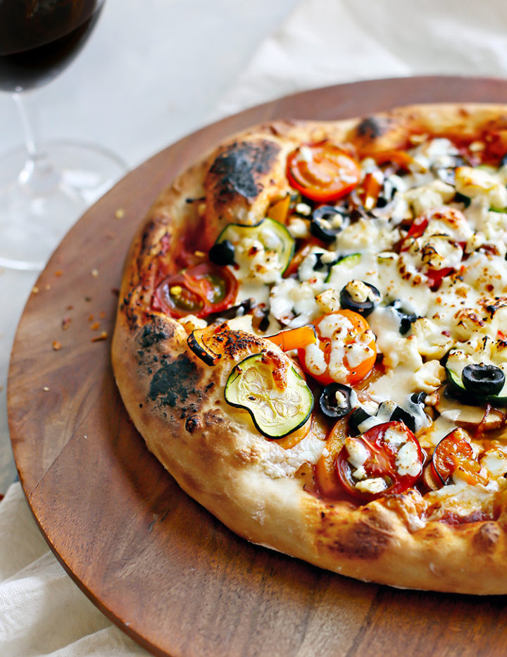 photo of veggie pizza on a wooden tray with a glass of wine
