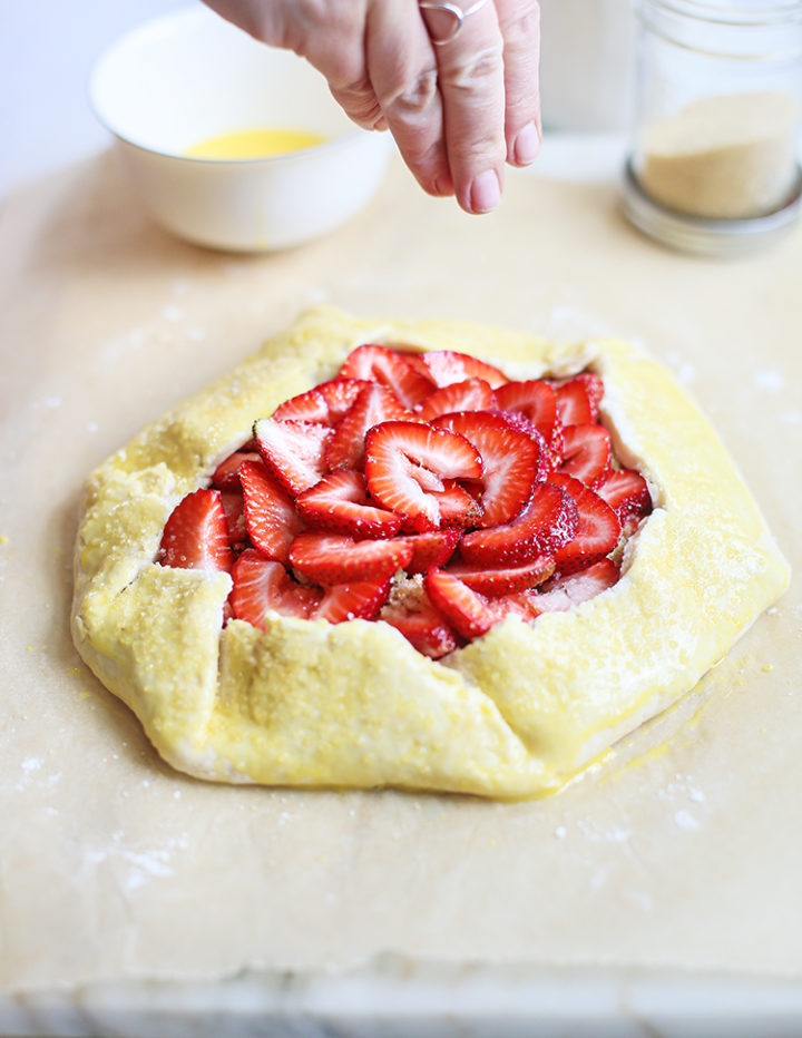 photo of woman sprinkling sugar on strawberry galette