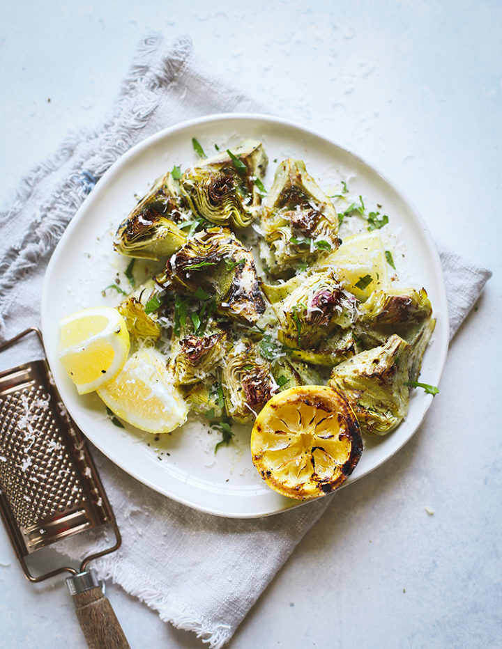 photo of a plate of grilled baby artichokes on a table with lemon and parmesan