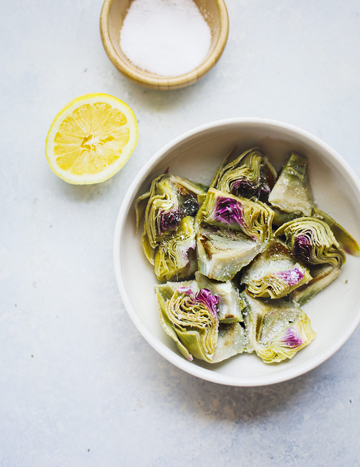 overhead photo of boiled baby artichokes in a bowl with a half of a lemon