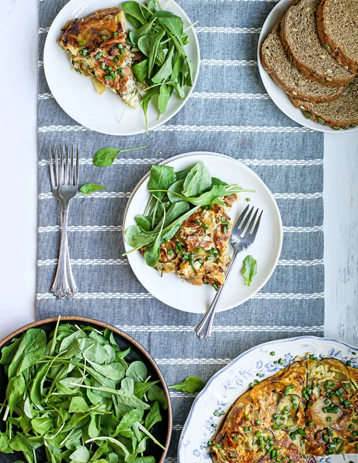 photo of several plates with slices of zucchini frittata on a table with spinach salad and toasts