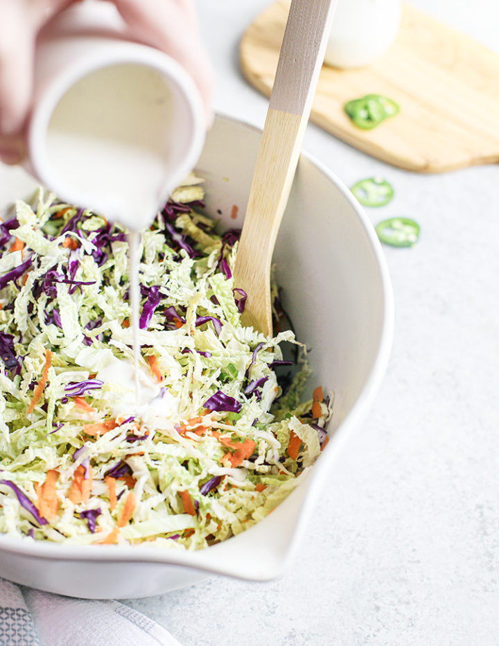 woman pouring jalapeño coleslaw dressing into the vegetables for the recipe