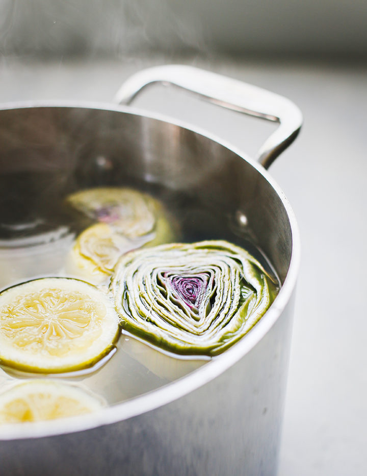 photo of baby artichokes simmering in a pot of hot water before being cooked on the grill