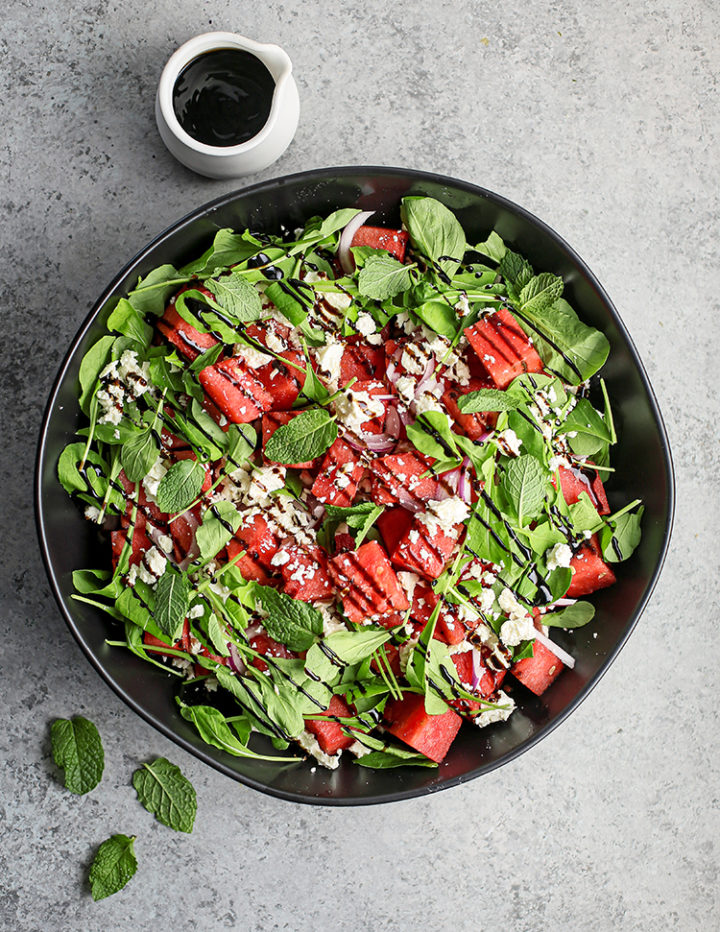 overhead photo of photo of watermelon feta mint salad with balsamic glaze in a black bowl 
