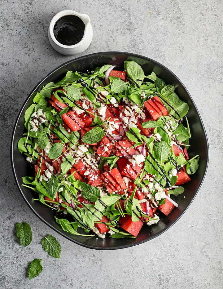 overhead photo of photo of watermelon feta mint salad with balsamic glaze in a black bowl
