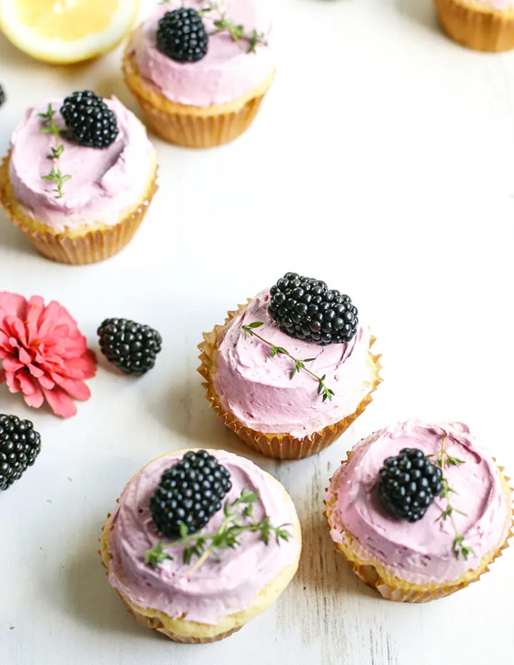 photo of lemon blackberry cupcakes on a white wooden table with lemons and flowers