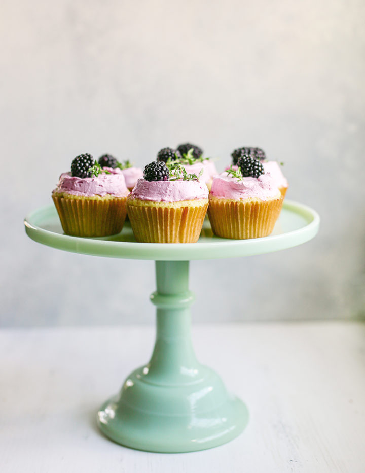 photo of blackberry cupcakes on a cake stand on a white wooden table