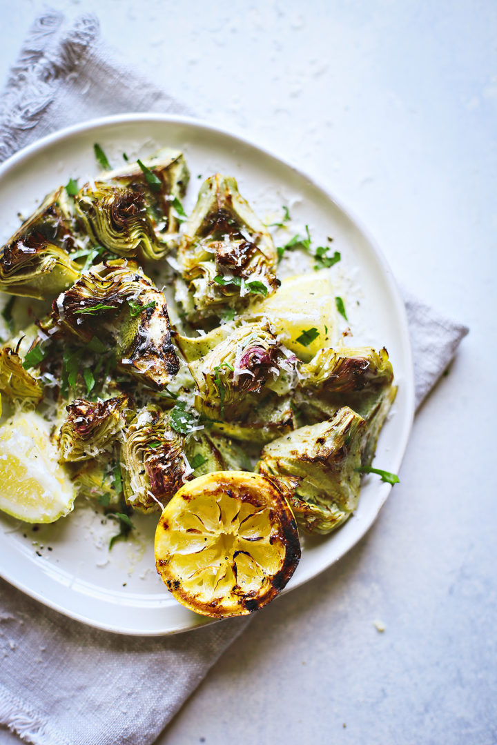 overhead photo of grilled baby artichokes on a plate with lemon and parmesan
