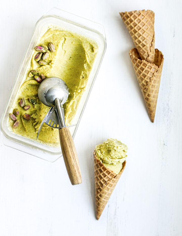 photo of pistachio gelato in a container being scooped into waffle cones