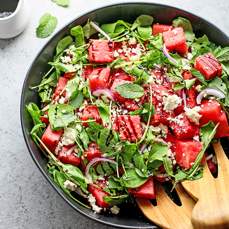 photo of watermelon feta mint salad in a black bowl with wooden salad tongs
