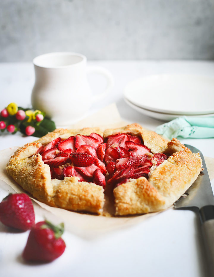 photo of a strawberry galette cut into slices with a knife and plates next to it