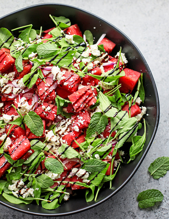 overhead photo of watermelon feta mint salad with balsamic glaze in a black bowl  