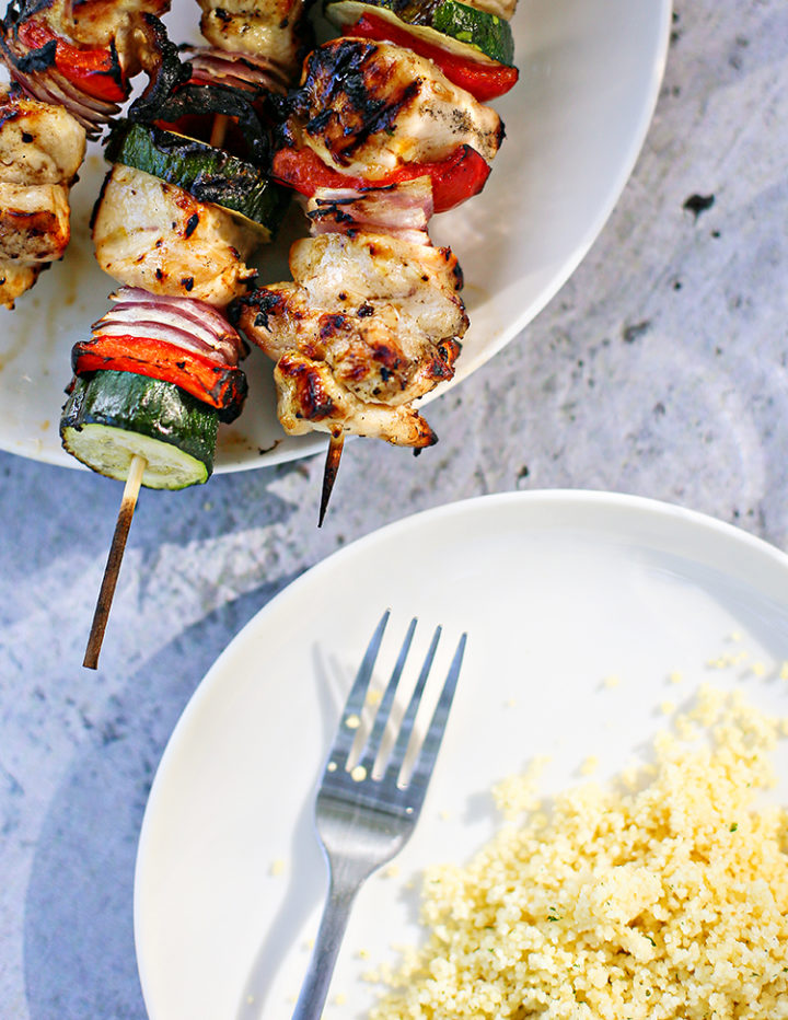 plates of couscous next to a plate with grilled chicken kebabs with a lemon honey garlic marinade