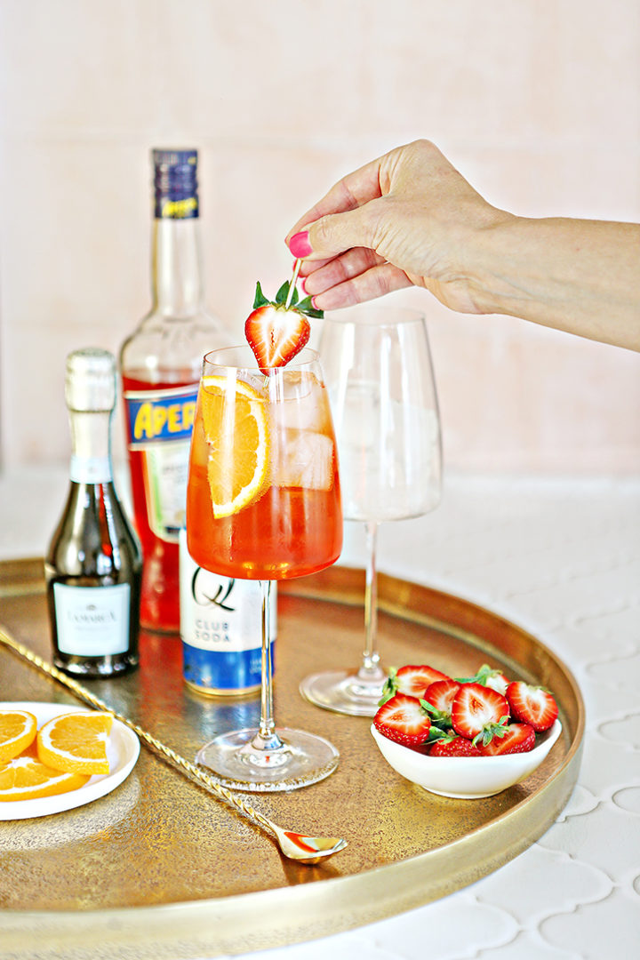 photo of a woman adding a strawberry garnish to a strawberry aperol spritz glass