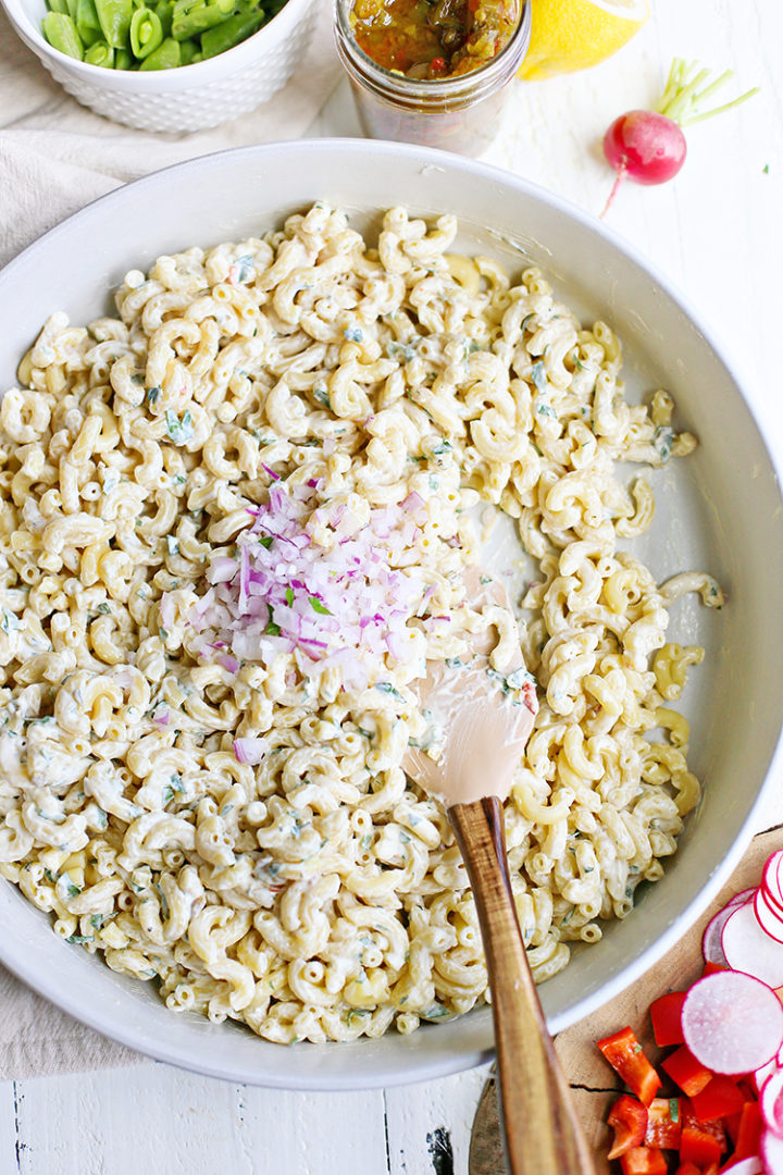 overhead photo of chopped red onion being stirring into a bowl of creamy macaroni salad 