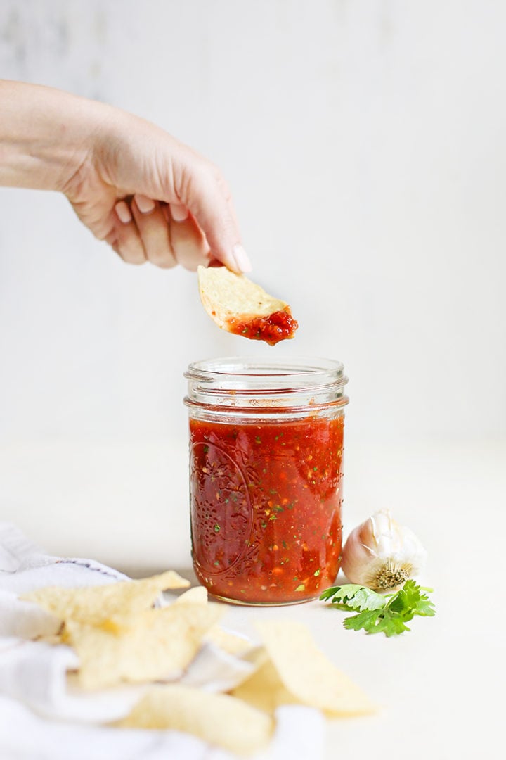 woman scooping salsa with a tortilla chip out of a jar of restaurant style salsa