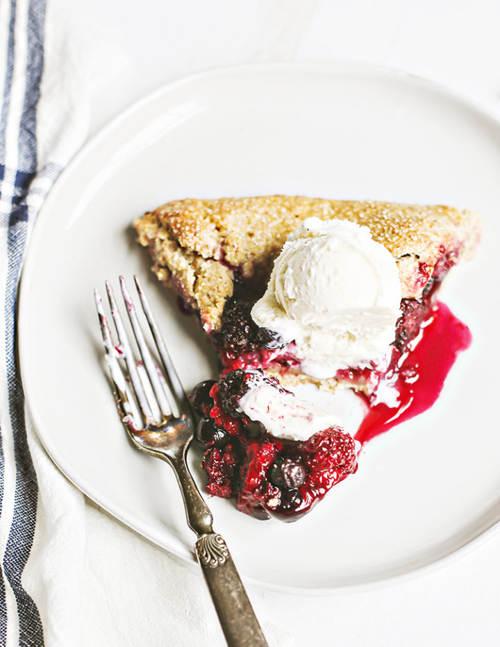 photo of a slice of mixed berry galette on a white plate with a scoop of ice cream