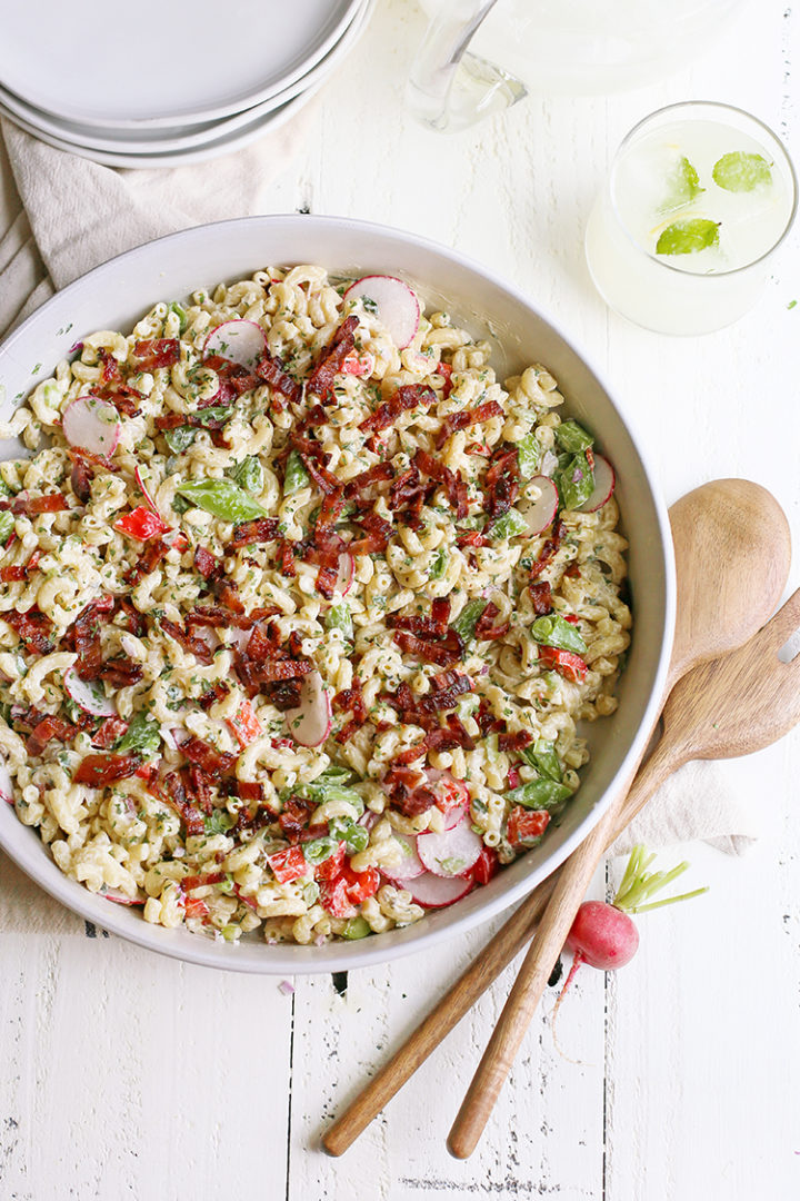 overhead photo of a large white bowl full of easy macaroni salad on a wooden table with serving spoons and plates