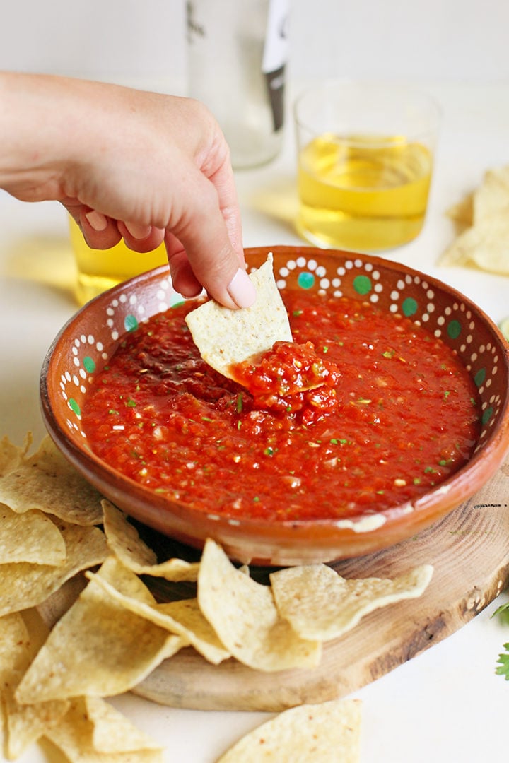 woman scooping a tortilla chip in a bowl of salsa restaurant style