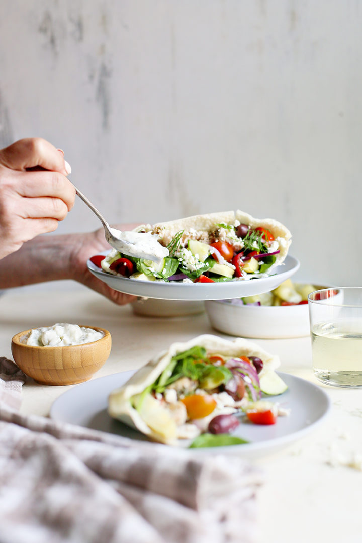 photo showing a woman putting homemade tzatziki sauce on a pita showing and example of how to serve tzatziki sauce recipe