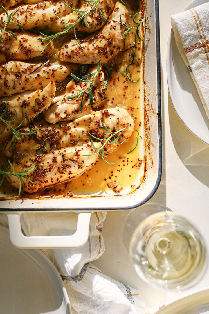 overhead photo of honey mustard chicken in a white baking dish garnished with rosemary sprigs