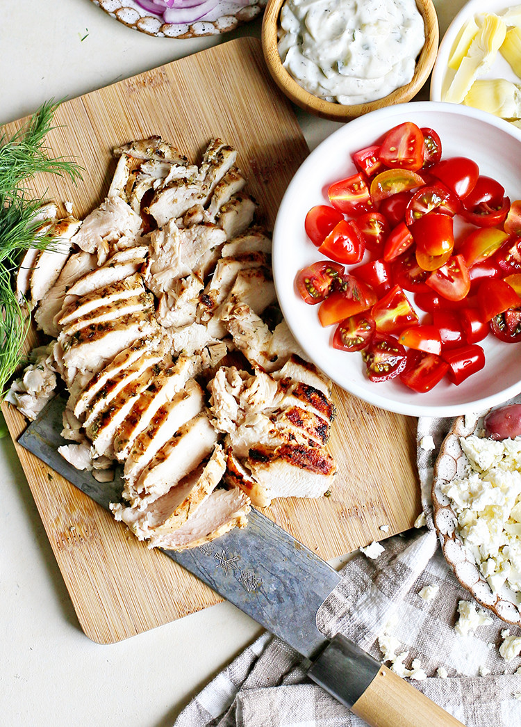 Sliced Greek chicken on cutting board with tomatoes