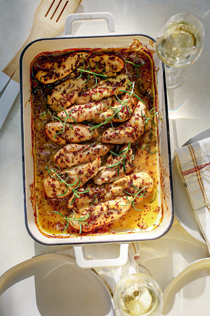 photo of a table set with plates, wine glasses, and a baking dish with honey mustard chicken