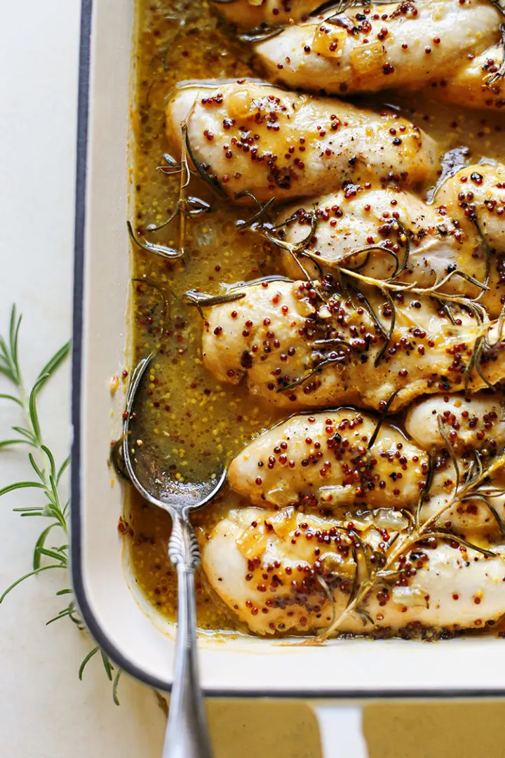 close up photo of baked honey mustard chicken in a white baking dish with a spoon