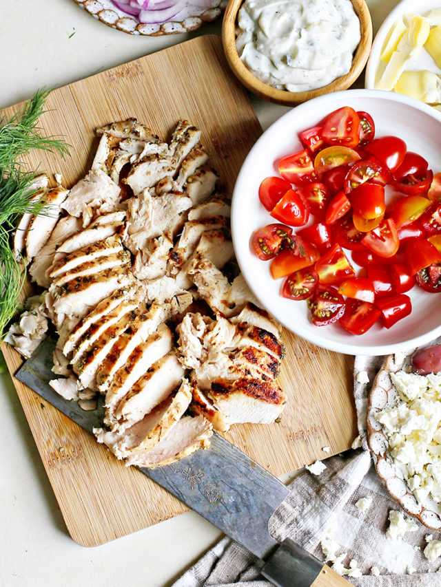 Sliced Greek chicken on cutting board with tomatoes