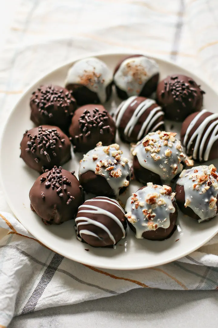 photo of a white plate full of chocolate and white chocolate dipped pumpkin truffles that have been decorated with sprinkles and nuts