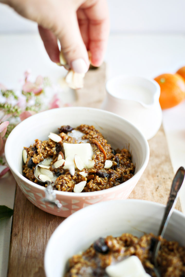 photo of a woman sprinkling sliced almonds onto a bowl of cherry oatmeal after making this recipe for overnight steel cut oats