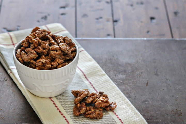 white bowl on a wooden table filled with glazed walnuts