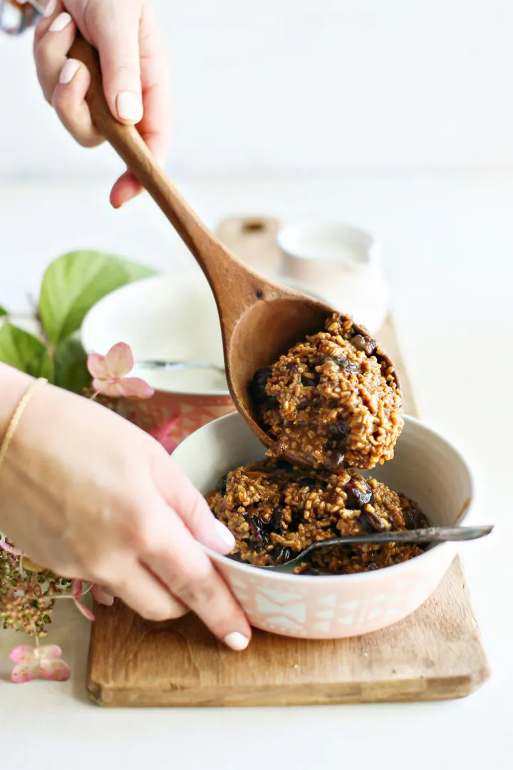 photo of a woman spooning cherry oatmeal into a bowl using a wooden spoon
