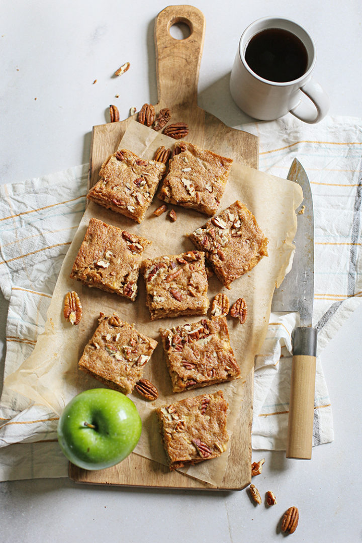 overhead photo of apple squares on a wooden cutting board with a knife and a mug of coffee