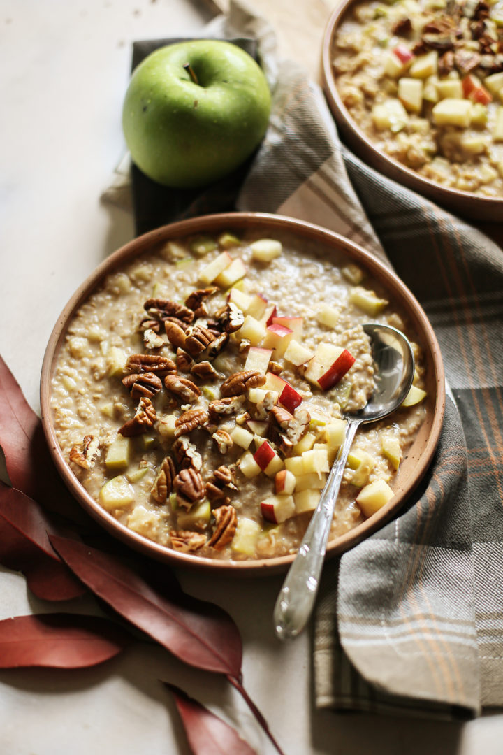 photo of a table set with two bowls of overnight apple oats, a plaid tablecloth, red leaves, and a green apple