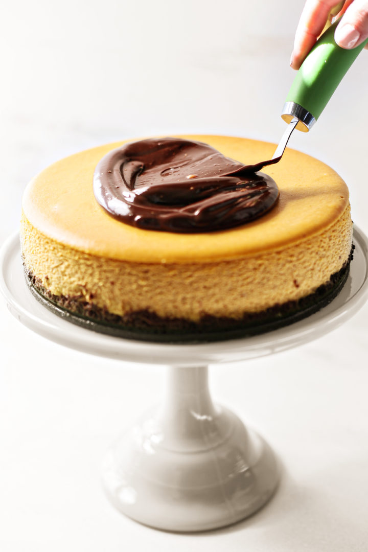 photo of chocolate ganache being spread on a chocolate pumpkin cheesecake