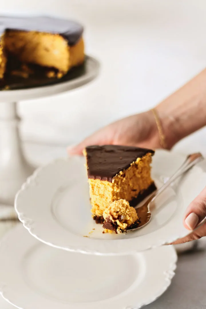 photo of woman holding a slice of pumpkin cheesecake on a white plate
