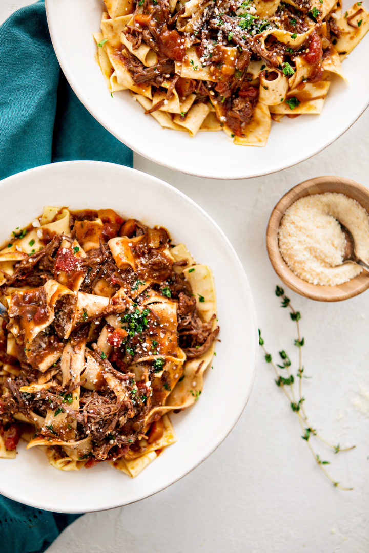 overhead photo of two white bowls of pappardelle pasta with shredded beef ragu sauce
