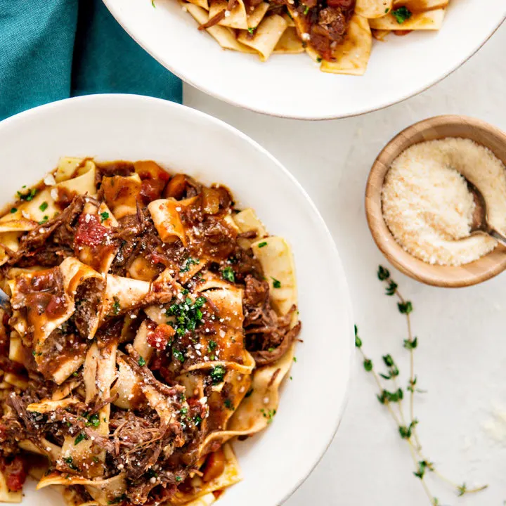 overhead photo of beef ragu served over pappardelle in white plates on a table