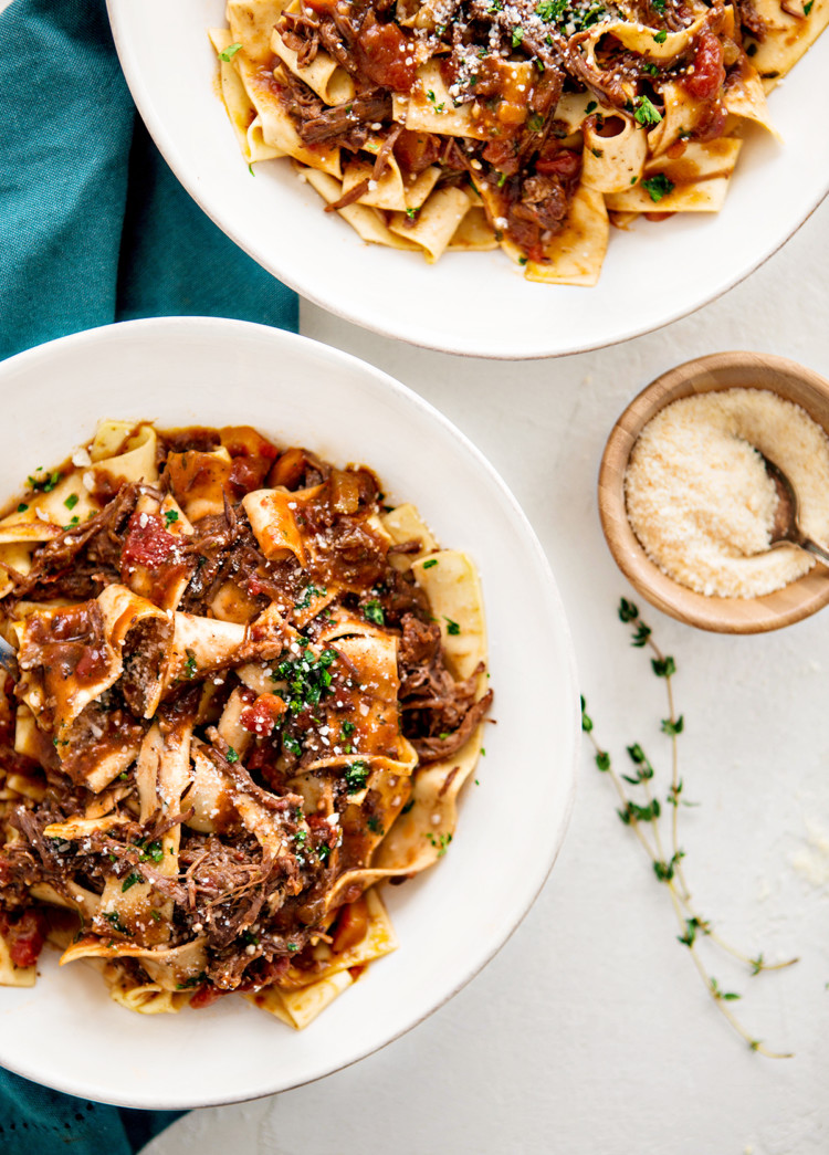 overhead photo of beef ragu served over pappardelle in white plates on a table