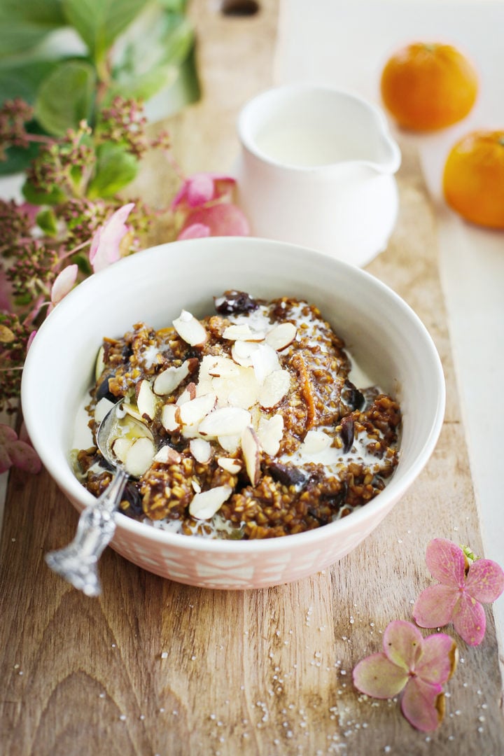 photo of a bowl of cherry oatmeal on a cutting board with a spoon from this recipe for overnight steel cut oats